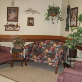 A cozy living room with floral and upholstered furniture, indoor plants, and wall decorations.