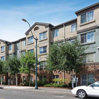 A residential apartment building with trees lining the street and a car parked nearby.