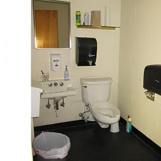 A small restroom with essential facilities, including a toilet, sink, mirror, and dispensers for soap and paper towels.