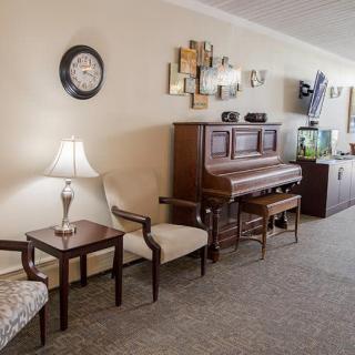 A cozy living room featuring a piano, comfortable chairs, and tasteful decor.