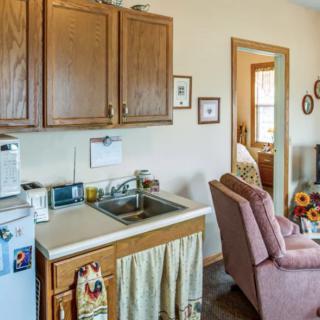 A cozy kitchen and living area featuring wooden cabinets, a sink, and a comfortable chair.