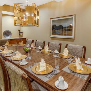 An elegantly set dining room with a long wooden table, ornate chandelier, and neatly folded napkins on each place setting.