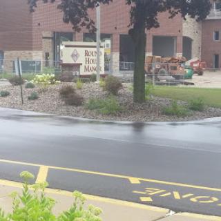 A view of a landscaped area with a sign, located near a building and road.