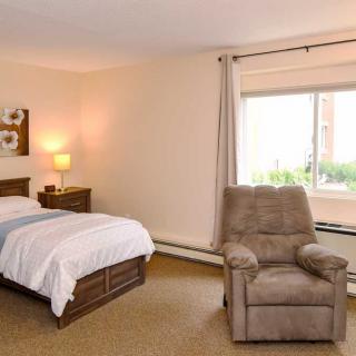 A cozy bedroom with a single bed, an armchair, and a large window.