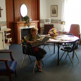 A person sits at a table reading in a cozy, well-lit room with a fireplace and flowers.