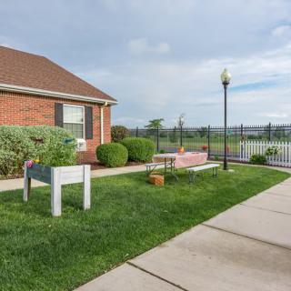 A brick house with a well-kept lawn, sidewalk, and lamp post next to a fence.
