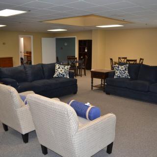 A spacious living room with comfortable seating, including couches and armchairs, arranged around a coffee table on a carpeted floor.