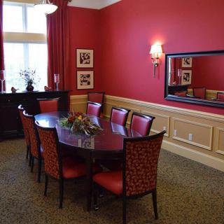 A formal dining room with red walls and matching chairs, featuring a large mirror and decorative wall art.
