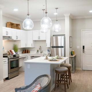 A modern kitchen featuring white cabinets, an island with bar stools, and stainless steel appliances under pendant lighting.