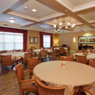 A warmly lit dining room with multiple tables and chairs arranged neatly beneath a chandelier.