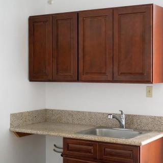 A small kitchen area with wooden cabinets, a granite countertop, and a stainless steel sink.