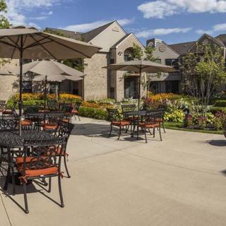 A sunny outdoor patio with tables, chairs, and umbrellas next to a landscaped building.