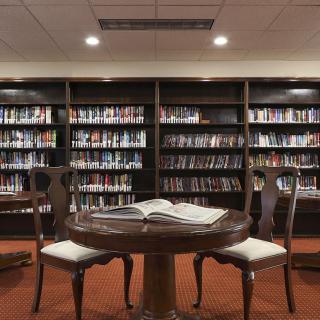A cozy library reading area with a round table and chairs surrounded by bookshelves.