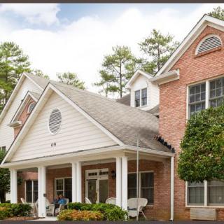 A charming suburban house with a brick facade and a welcoming porch surrounded by trees.