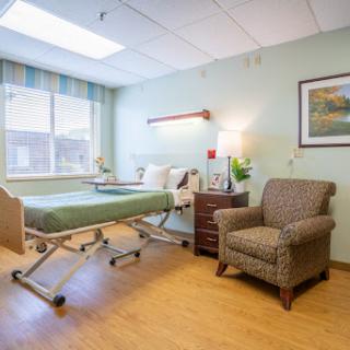A well-lit hospital patient room featuring a bed, comfortable chair, and window.