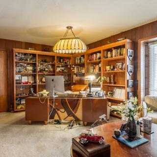 A cozy home office with wooden bookshelves and a central desk, featuring ample natural light.