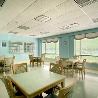 An empty dining room with multiple tables and chairs, illuminated by natural daylight through large windows.
