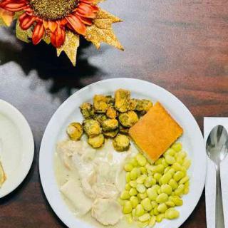 A dinner plate featuring turkey with gravy, Brussels sprouts, lima beans, and cornbread, accompanied by a slice of bread.