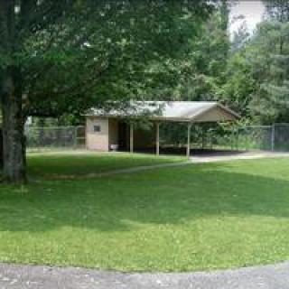 A small shed in a park surrounded by trees and a grassy area.