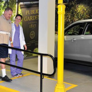 A nurse assists a patient as they walk towards a vehicle in a hospital parking area.