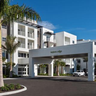 A modern apartment complex with palm trees and a welcoming entrance under a clear blue sky.