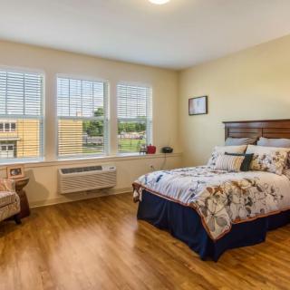 A well-lit bedroom with large windows, featuring a comfortable bed and cozy furnishings.