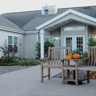 A cozy house entrance adorned with pumpkins and plants, featuring wooden benches on the porch.