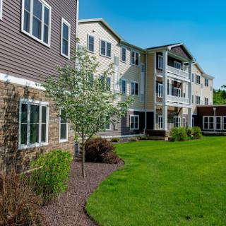 A beautifully landscaped apartment building with a well-maintained lawn under a clear blue sky.