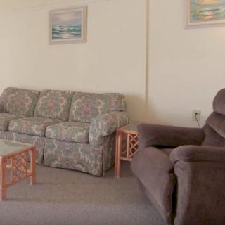 A cozy living room featuring a patterned sofa, an armchair, and a wooden coffee table, adorned with wall paintings.