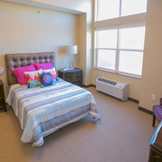 A cozy bedroom with a bed, colorful pillows, and large windows.