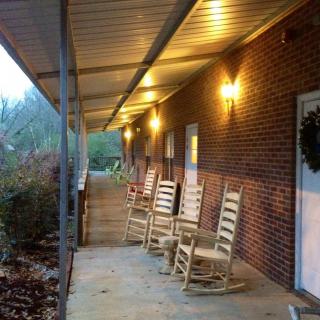 A cozy porch with rocking chairs lined up along a brick building, illuminated by warm outdoor lights.