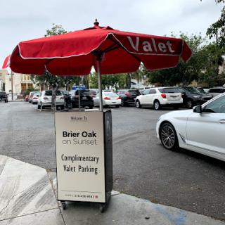 A valet service sign offering complimentary parking, situated under a red umbrella on a city street.