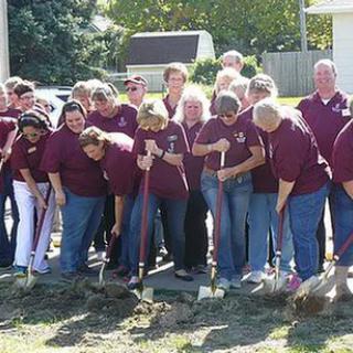 A group of people participating in a groundbreaking ceremony using shovels outdoors.