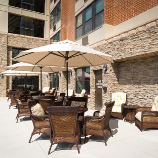 An outdoor patio area with wicker furniture and large umbrellas, adjacent to a building with a brick exterior.
