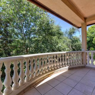 A sunny balcony with a tiled floor and decorative railing overlooking lush green trees.