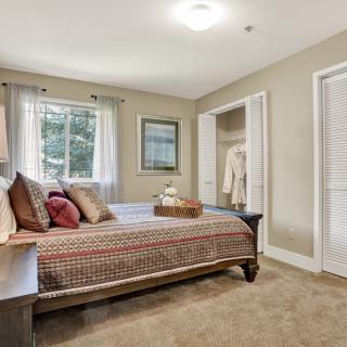 A cozy bedroom with a neatly made bed, soft carpeting, and natural light from the window.