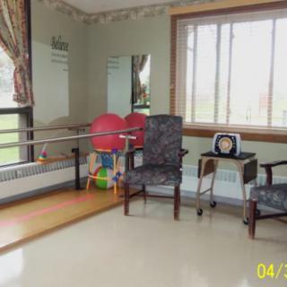 A rehabilitation room featuring chairs, exercise equipment, and a large window.