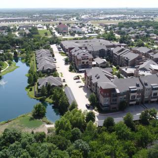 Aerial view of a residential area with modern buildings, surrounded by greenery and a water body.