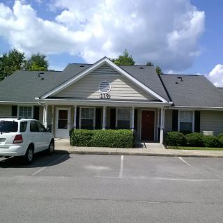 A small office building with a parking lot and a car parked in front under a partly cloudy sky.