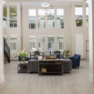 A modern living room with high ceilings and large windows, furnished with blue chairs and neutral tones.