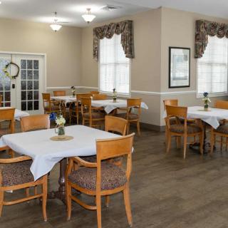 A cozy dining area with neatly arranged tables and chairs, featuring large windows and elegant decor.