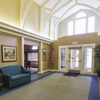 A well-lit lobby with a vaulted ceiling, featuring a sofa, artwork on the walls, and an entrance area.