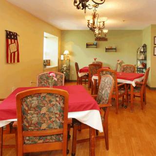 A cozy dining room with multiple tables set with red tablecloths and patterned chairs, illuminated by a chandelier.