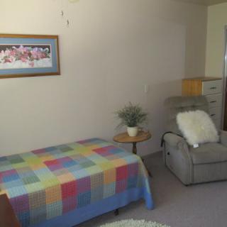 A cozy bedroom with a colorful quilt, reclining chair, and decorative elements.
