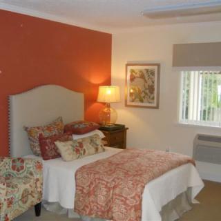 A cozy bedroom with warm-toned decor and a comfortable bed next to a lamp and painting.