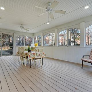 A spacious porch with a dining area, featuring ceiling fans and wood flooring, surrounded by windows.