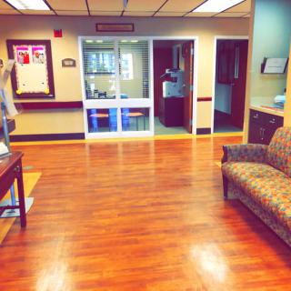 An empty hospital waiting room with wooden floors and patterned seating.
