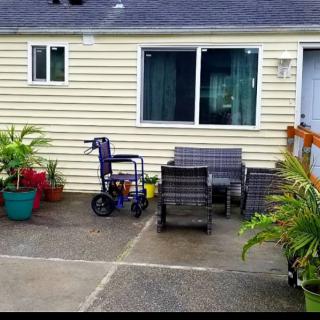 A patio area with outdoor furniture and a wheelchair next to potted plants outside a house.