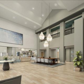 A modern and spacious lobby featuring elegant lighting fixtures, a reception desk, elevators, and decorative plants.