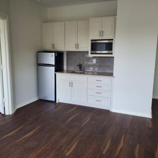 A small, modern kitchen in an apartment with wood flooring and white cabinets.